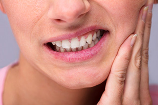 Femme se tenant la mâchoire avec une expression de douleur, illustrant un problème de bruxisme ou de tension au niveau de la mâchoire.